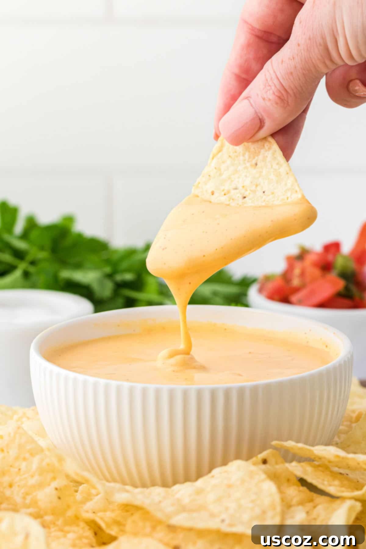 Plant-Powered Mexican Feasts 2 dipping a chip into nacho cheese sauce, showcasing its creamy texture