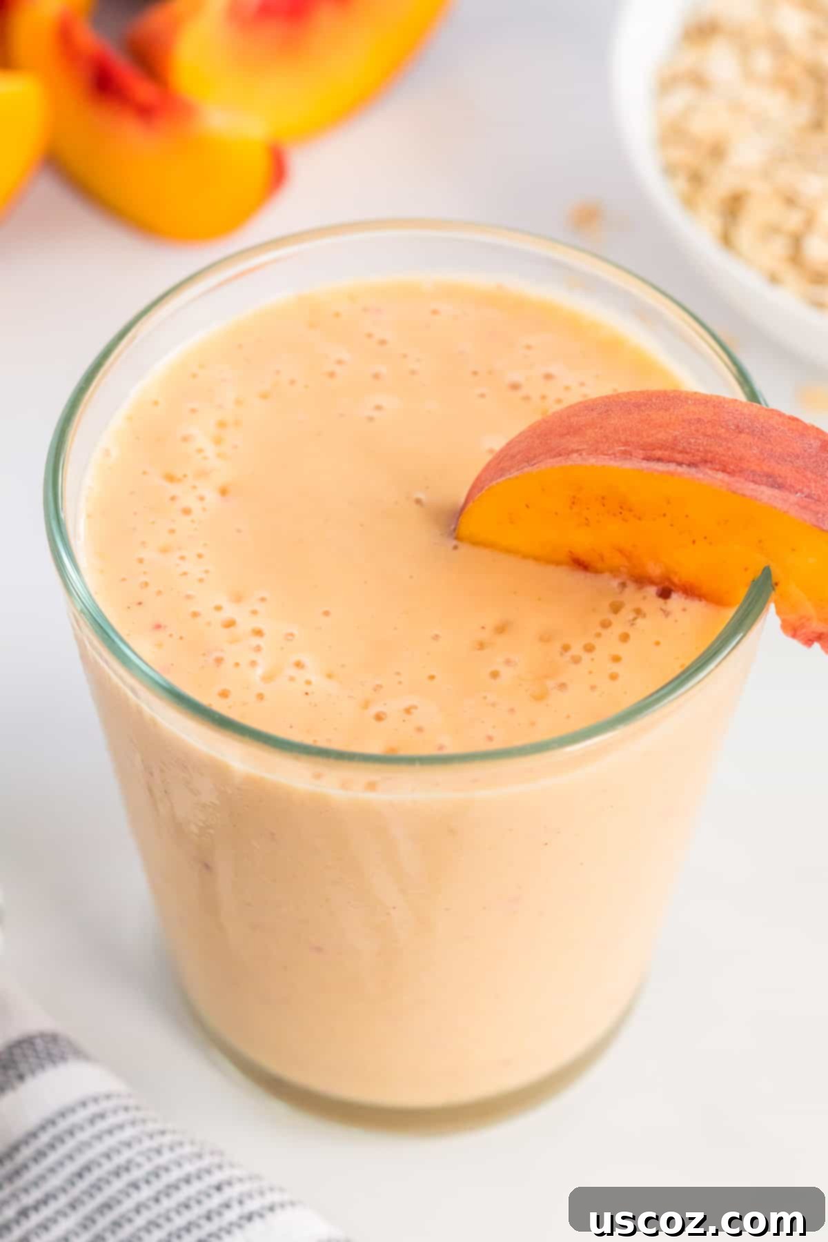 Wholesome Peach Smoothie 6 A refreshing, healthy peach smoothie in a glass, garnished with a peach slice on the rim, showcasing its creamy texture.