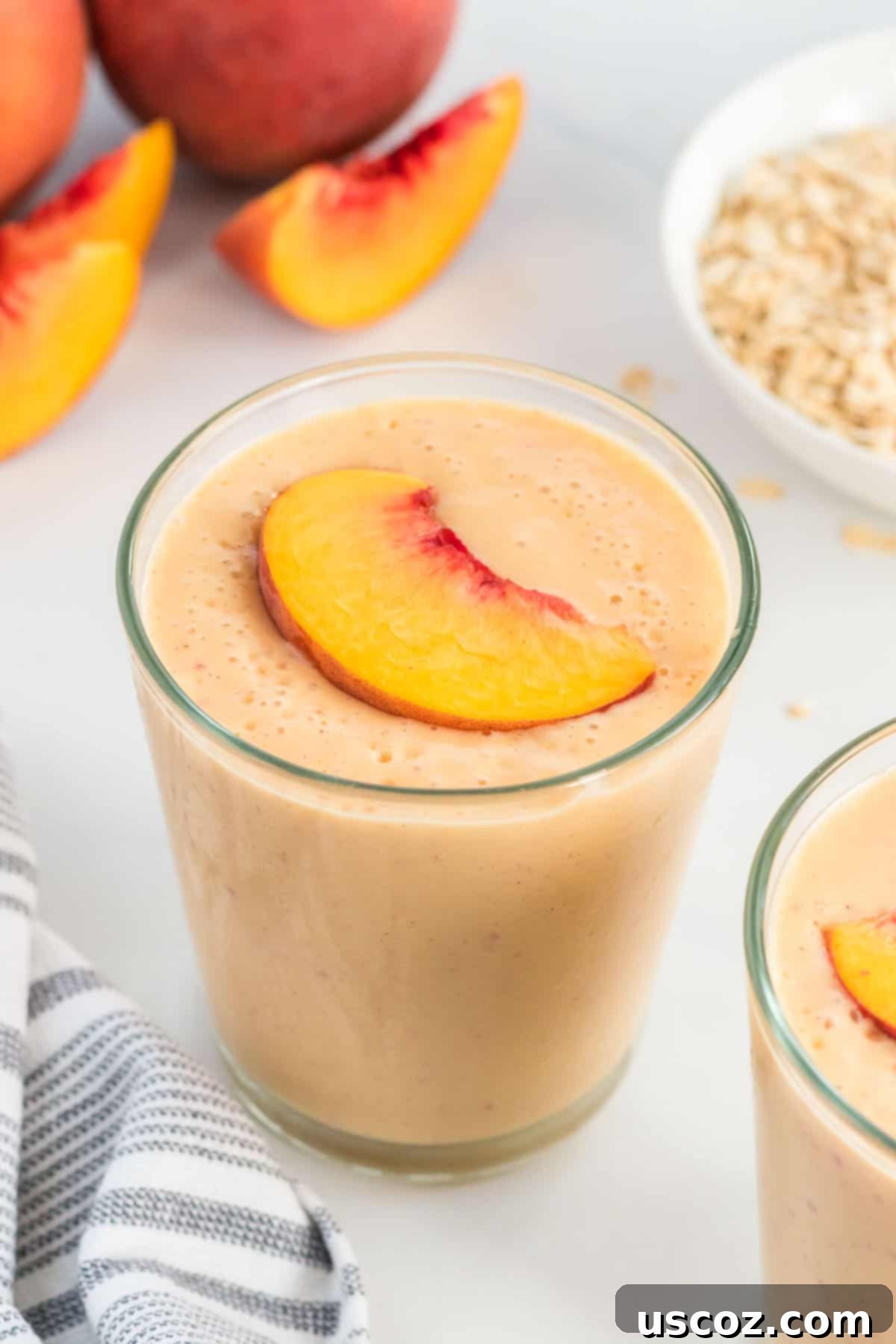 Wholesome Peach Smoothie 7 Two glasses of creamy peach smoothies topped with fresh peach slices and a sprinkle of cinnamon, ready to be enjoyed.