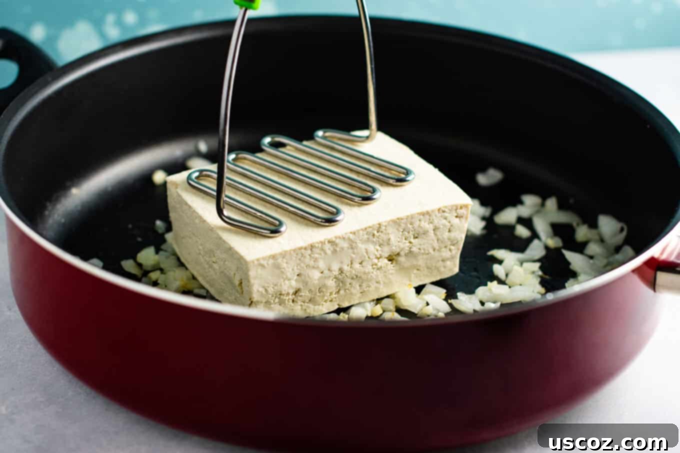 Wholesome Tofu Scramble 4 Extra-firm tofu being broken into egg-like pieces with a potato masher in a skillet for a vegan scramble. #easytofuscramble #veganbreakfast