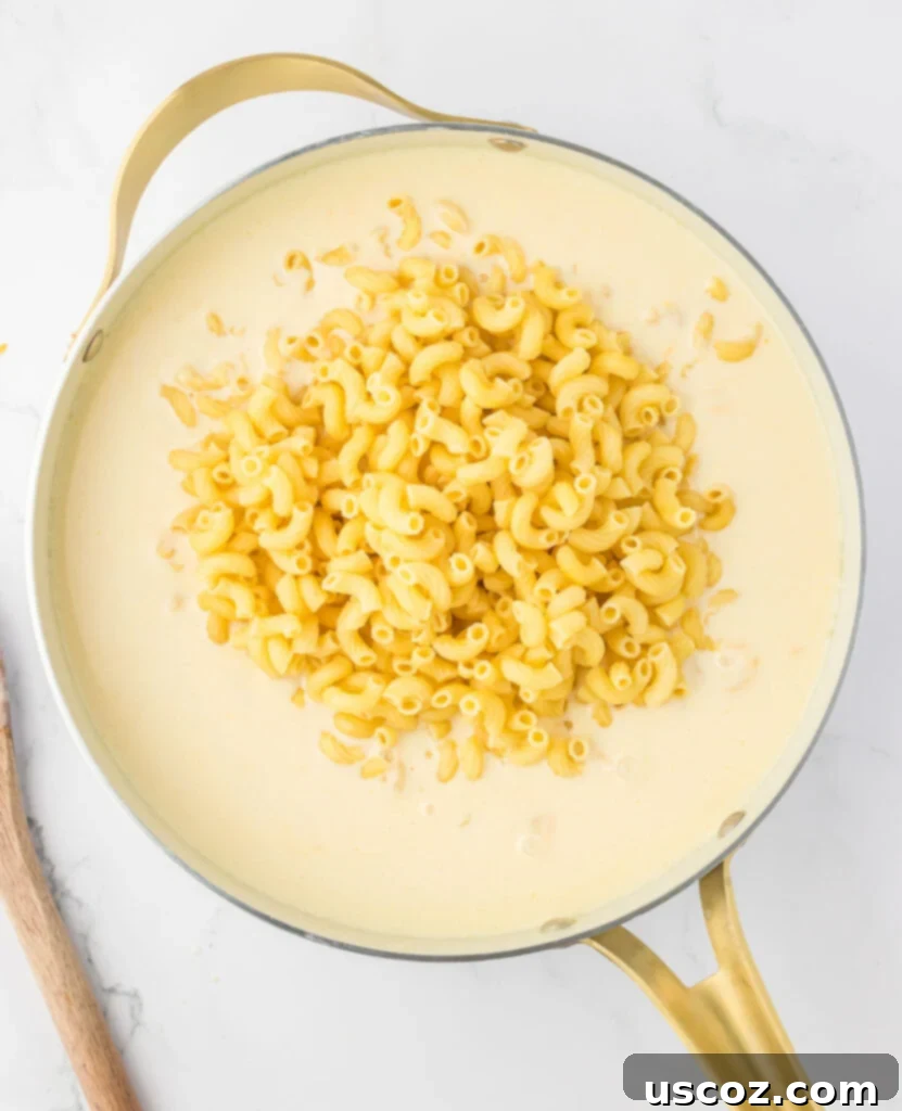Golden Baked Macaroni Perfection 10 adding macaroni noodles to the cheese sauce