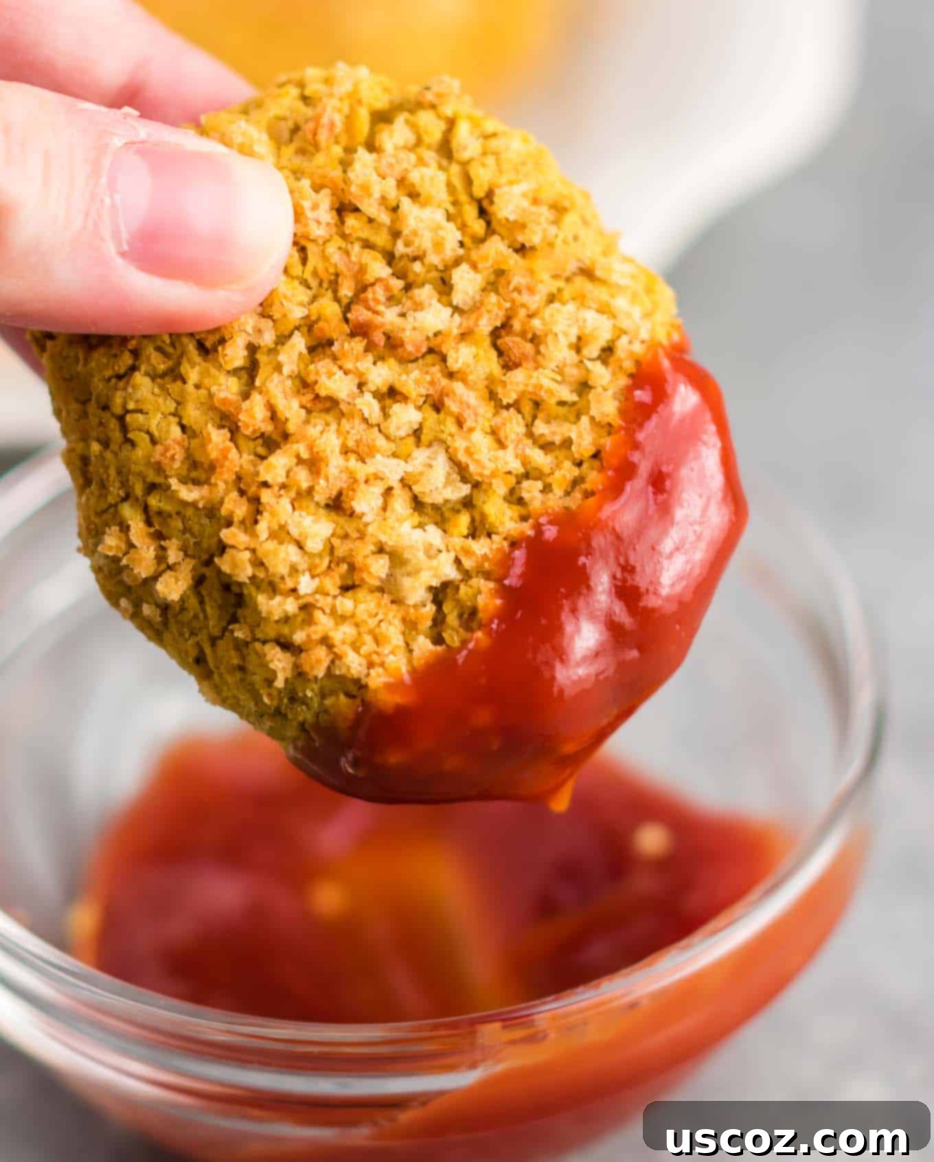 Golden Chickpea Poppers 7 A golden-brown vegetarian chickpea nugget being dipped into a swirl of red ketchup, highlighting its crispy texture.