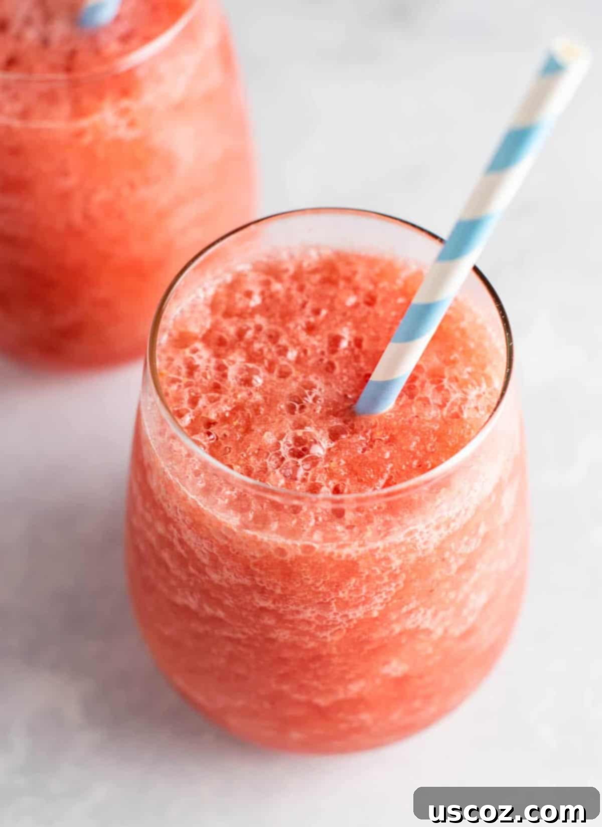 Two glasses of vibrant pink watermelon white wine slushies, garnished with fresh mint, sitting on a wooden table outdoors. The perfect summer alcoholic drink to beat the heat.