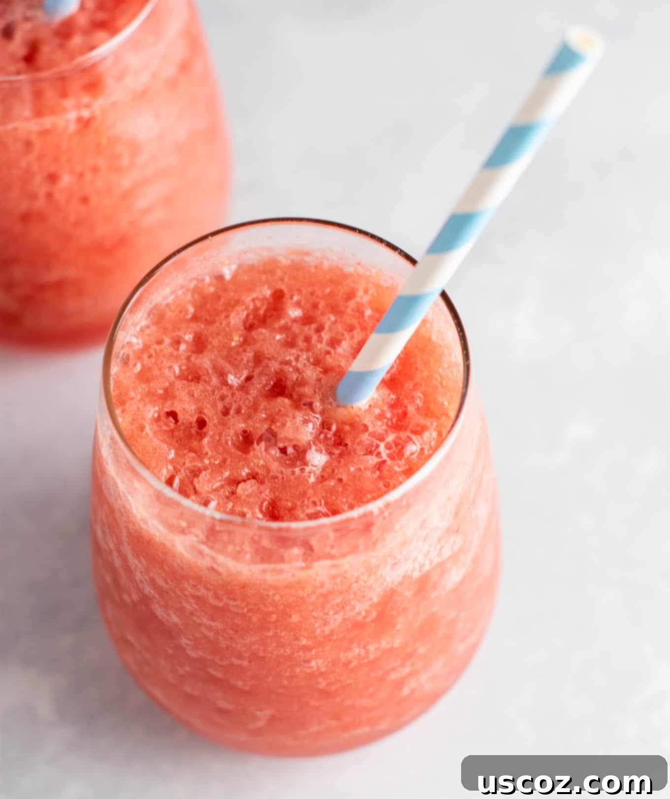 A top-down view of two watermelon white wine slushies in glasses, surrounded by fresh watermelon slices and mint sprigs.