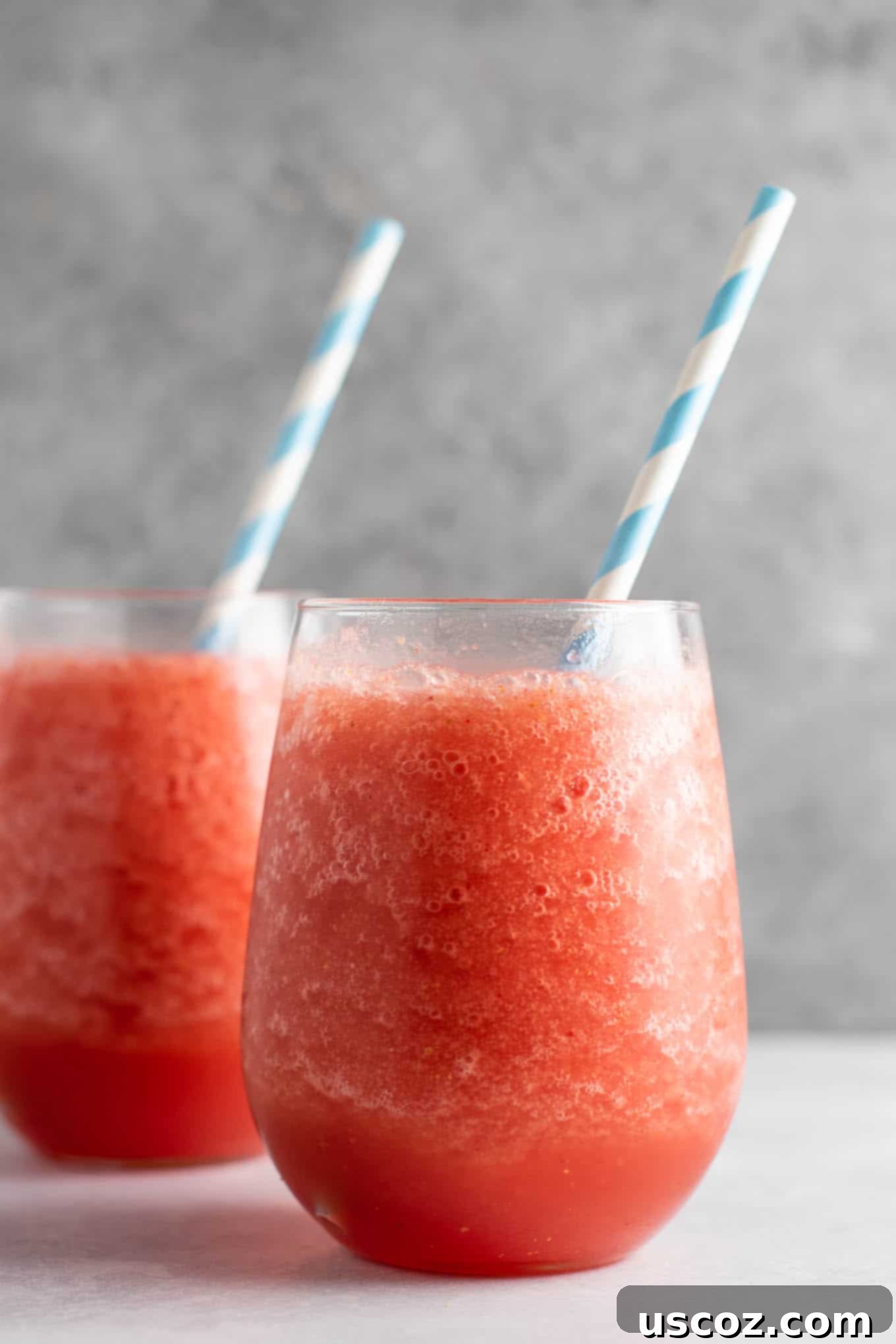 Close-up of a watermelon white wine slushie in a stemmed glass, highlighting the icy texture and garnished with a fresh watermelon wedge. A perfect frozen summer cocktail.