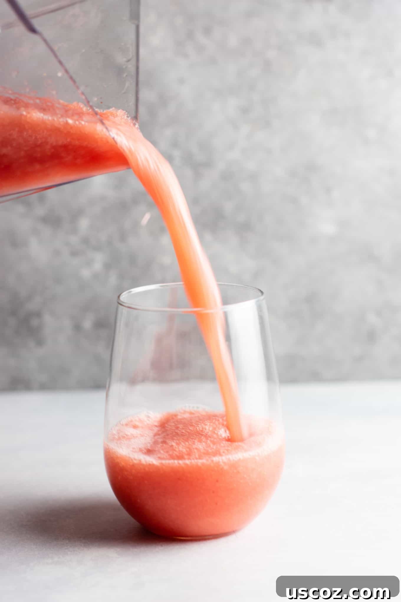 Multiple glasses of watermelon white wine slushies on a rustic wooden surface, with a pitcher in the background, set for a summer gathering.