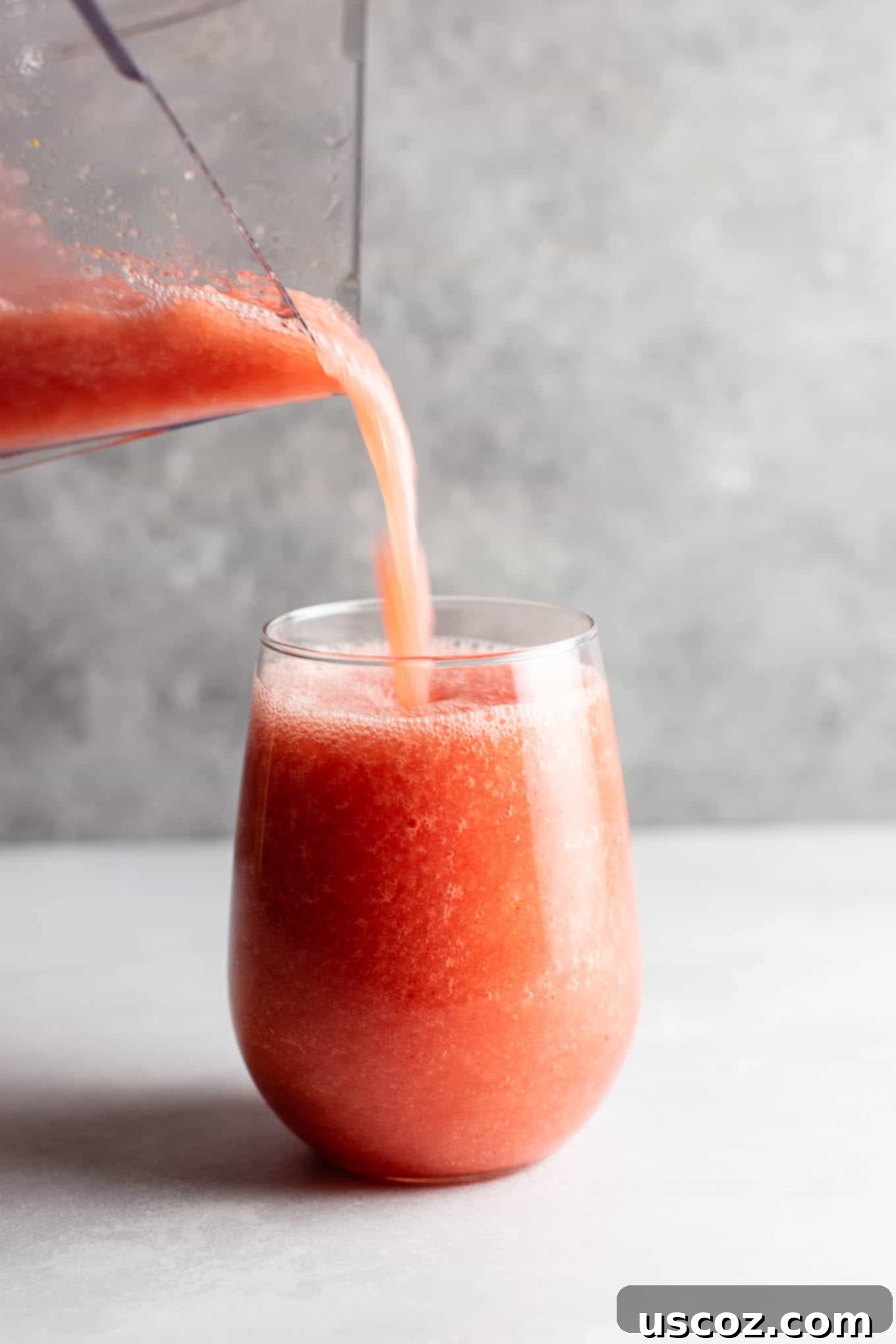 A close-up shot of a watermelon white wine slushie being garnished with a fresh watermelon triangle and a sprig of mint.