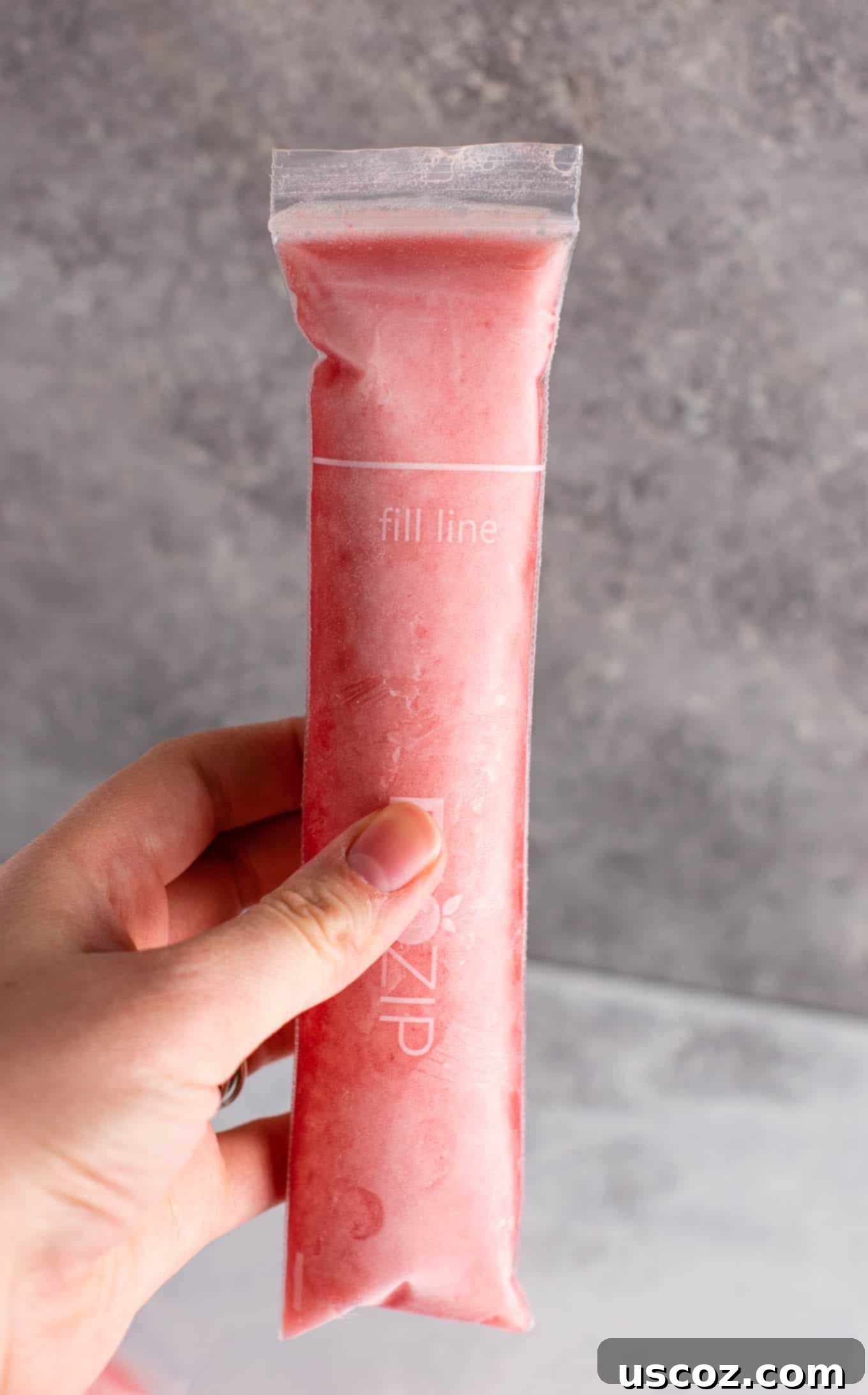 A close-up of a partially eaten Strawberry Pineapple Freezer Pop, showing its icy texture and bright colors against a sunny background, emphasizing its refreshing qualities.