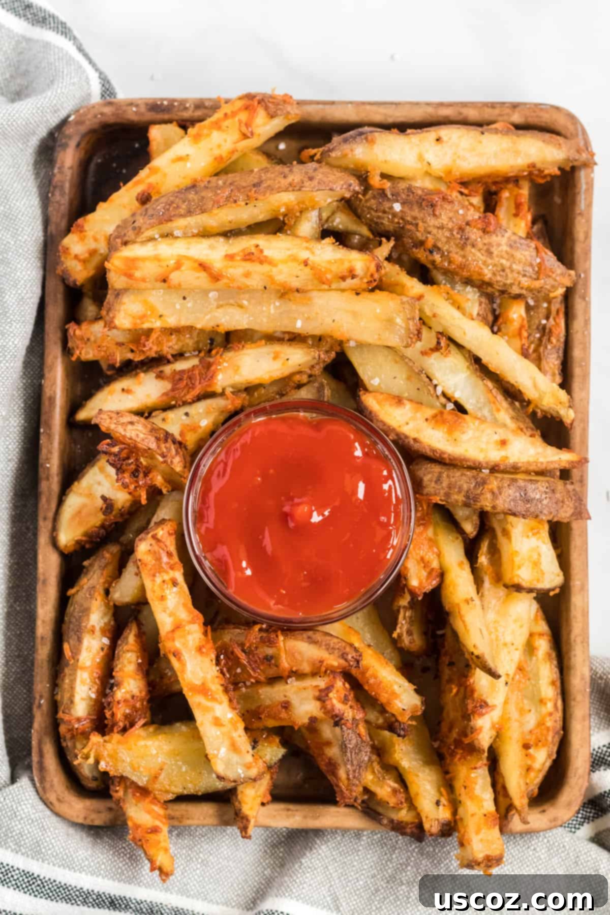 Garlic Parmesan Baked Potato Wedges 2 Golden brown crispy oven baked garlic parmesan potato wedges on a rustic brown serving tray with a small white bowl of ketchup in the center, ready to be enjoyed as a perfect snack or side.