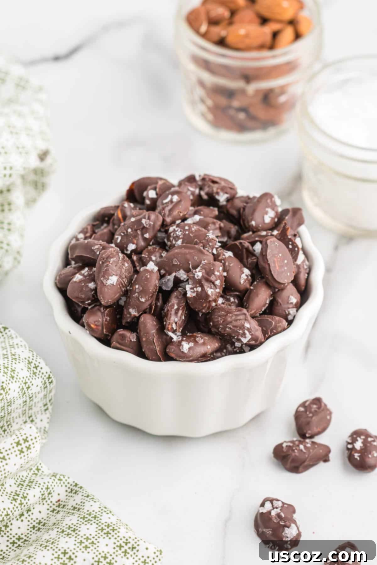 25 Decadent Gluten-Free Dairy-Free Desserts 26 A white bowl filled with glistening chocolate-covered almonds sprinkled with sea salt, highlighting their simple elegance.
