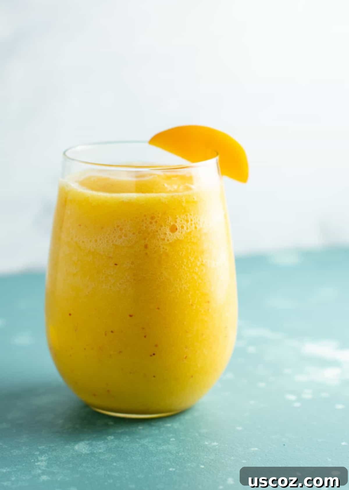 Two glasses of vibrant peach moscato slushies garnished with fresh peach slices, ready for a refreshing summer sip. Ideal for healthy summer drinks and parties.