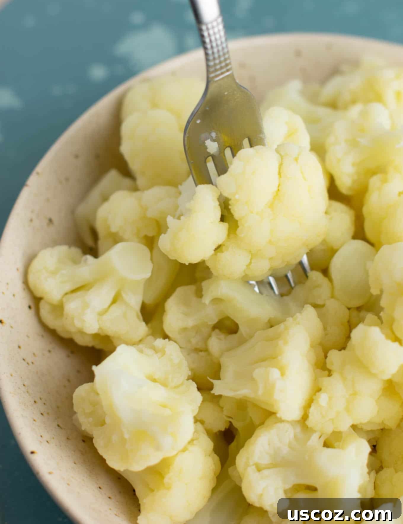 Perfectly Steamed Cauliflower 9 A fork taking a piece of perfectly steamed cauliflower from a white bowl, showing its tender texture.