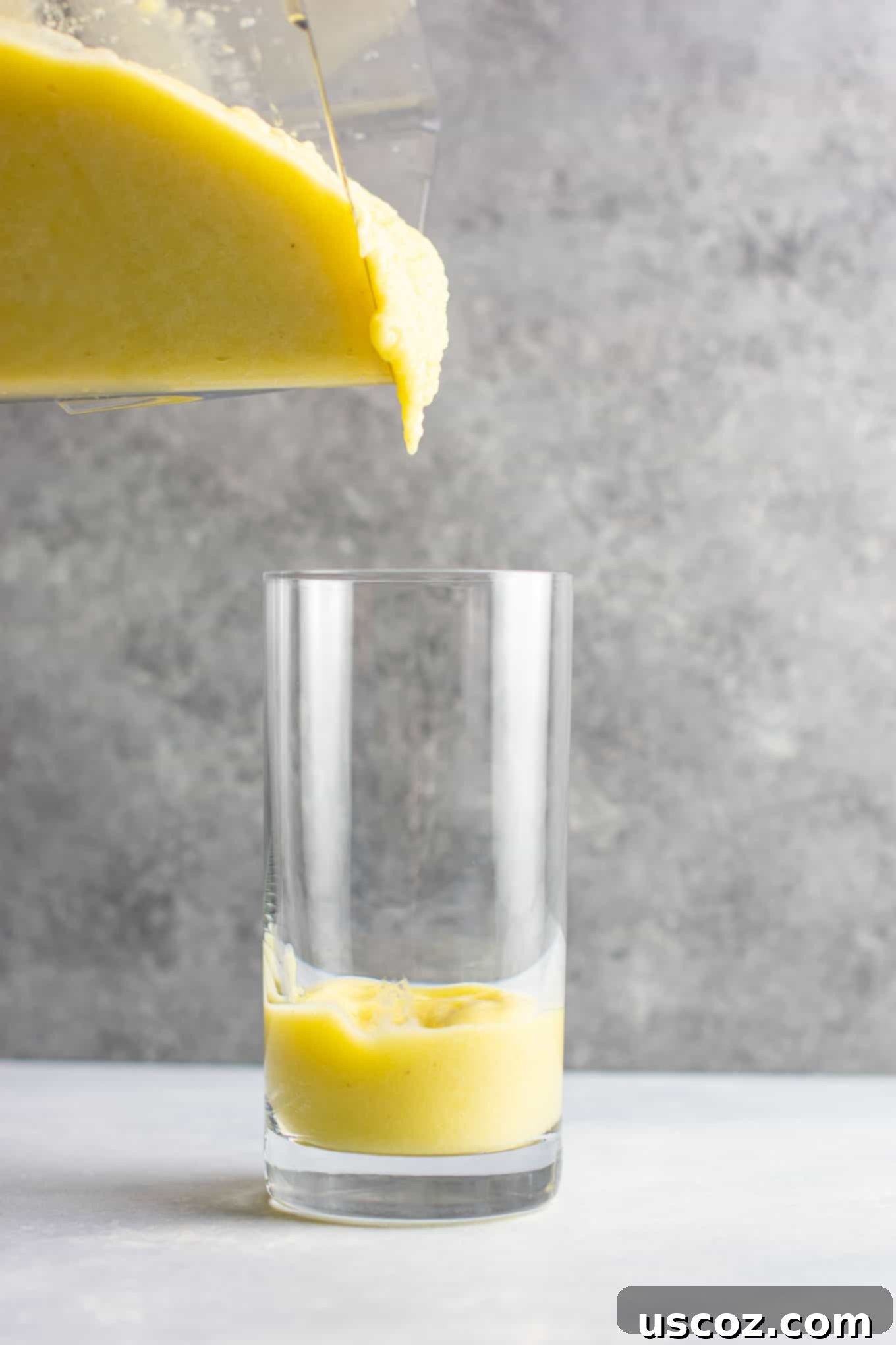 Pineapple Detox Blast 9 A tall glass filled with a creamy pineapple detox smoothie, garnished with a fresh pineapple slice and a mint sprig, against a light background.
