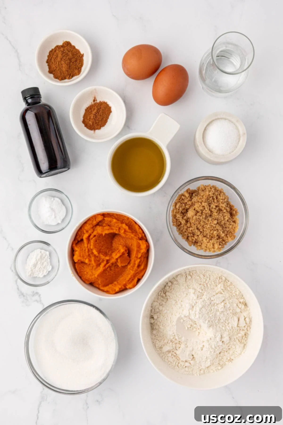 A selection of fresh ingredients laid out for making pumpkin bread, including flour, pumpkin puree, eggs, oils, and spices.
