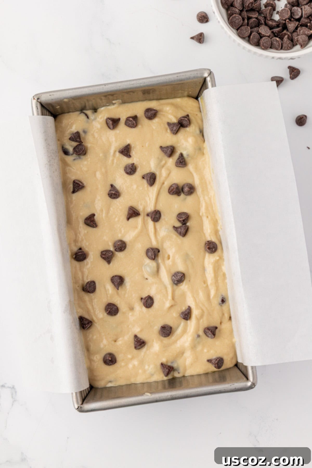 Loaf pan with batter and extra chocolate chips sprinkled on top, ready for baking