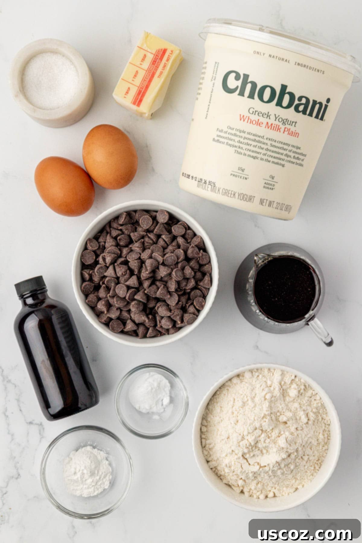 Various ingredients for Greek yogurt quick bread laid out on a counter, including yogurt, eggs, butter, flour, and chocolate chips