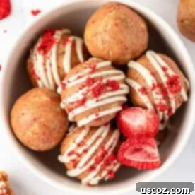 Vibrantly pink strawberries and cream energy bites, artfully drizzled with white chocolate
