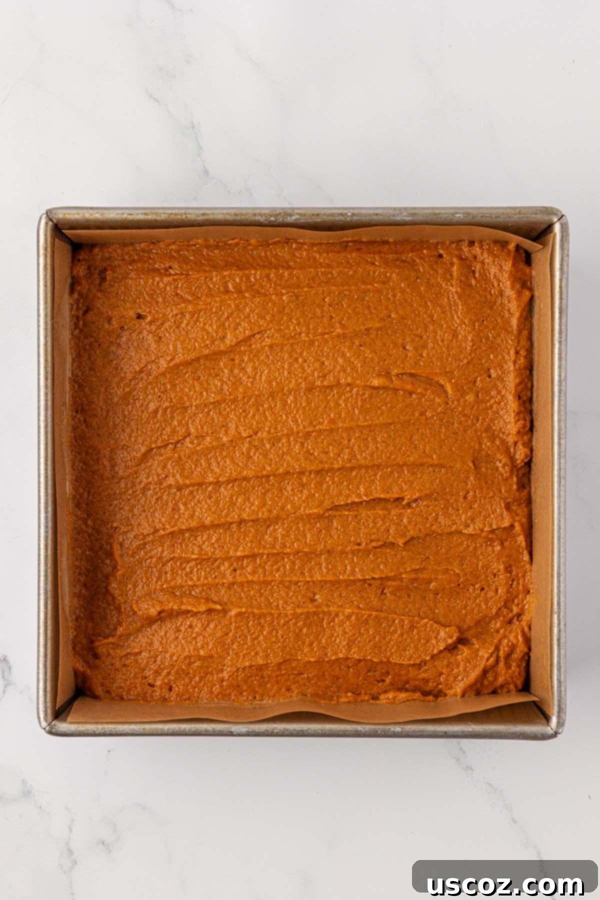 Pumpkin bread batter spread out in an 8x8 inch baking pan, ready for the oven