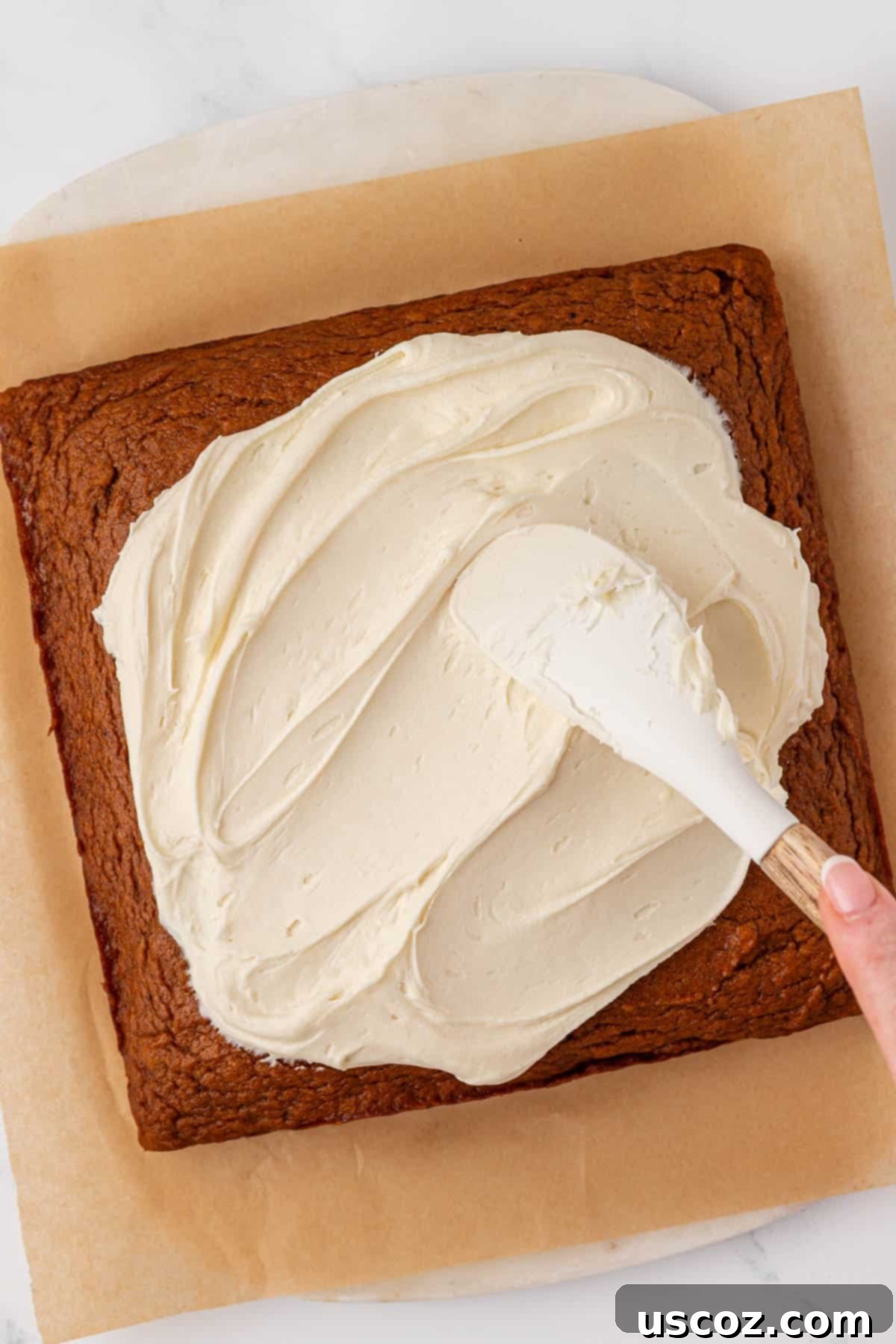 Spreading cream cheese frosting evenly onto the cooled pumpkin cake