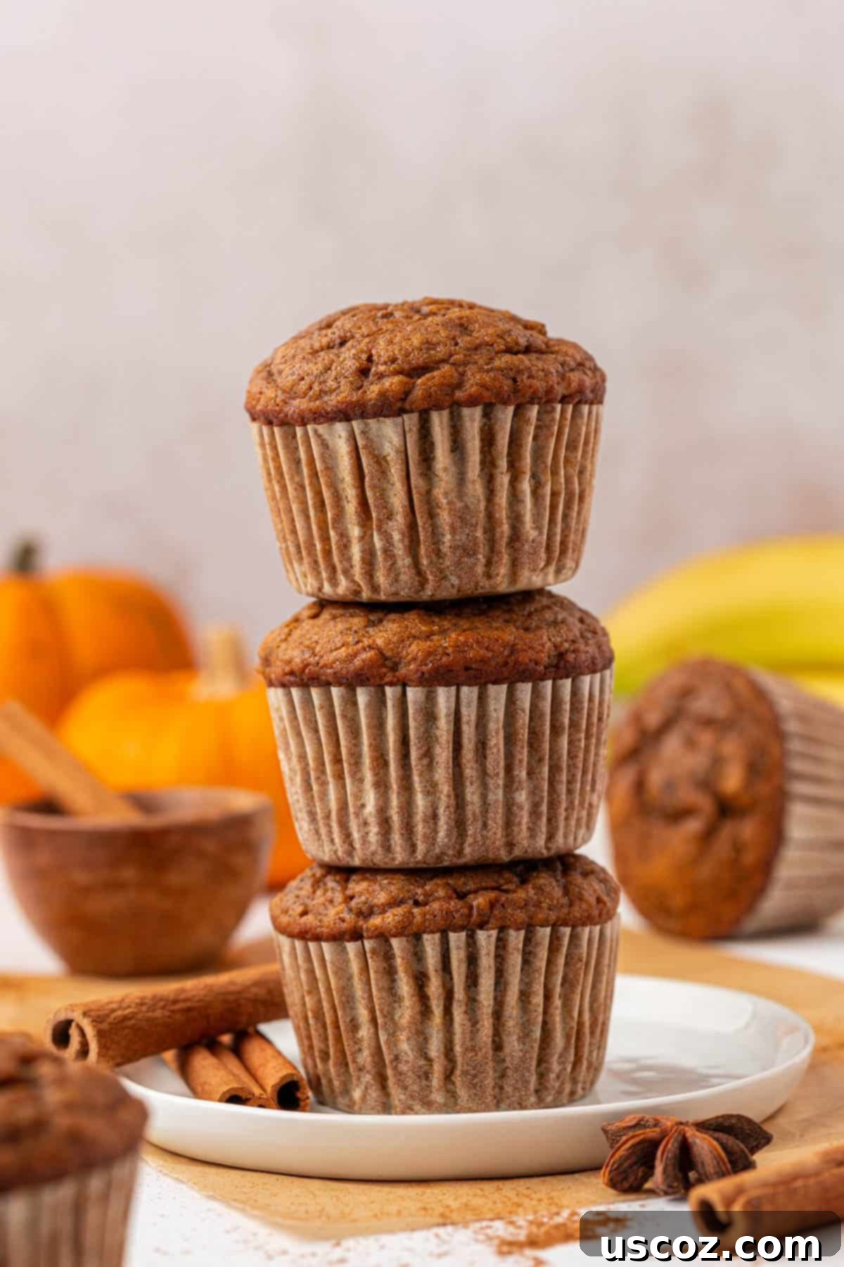 Golden Pumpkin Banana Muffins 3 stacked pumpkin banana muffins on a wooden board